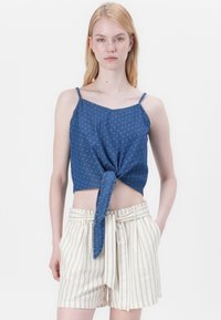 Top court en denim avec de petits pois blancs, noué à l'avant ; associé à un short taille haute à rayures crème et beige. Texture lisse.