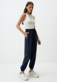 Marineblauwe casual broek met elastische tailleband en boorden. Gekleed met een wit mouwloos topje en witte sneakers. Soepele stof textuur.
