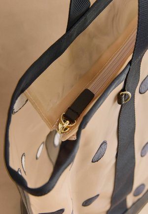 Smėlio spalvos rankinė su juodais taškeliais, juoda apdaila, medžiaginėmis rankenomis ir smėlio spalvos vidine kišene su auksiniu užtrauktuko laikikliu.