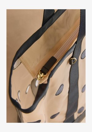 Beżowa torba na ramię w czarne kropki, z czarną lamówką, materiałowymi uchwytami oraz beżową kieszenią wewnętrzną na zamek z złotym suwakiem.