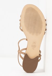 Sandale en cuir marron avec des brides fines et une semelle texturée. Couleur miel notable avec un logo imprimé sur la semelle intérieure. Design à talon plat.
