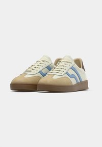 Krém és barna tornacipők kék csíkokkal, velúr és bőr anyagokból, fűzős kivitel, gumi talp és megerősített sarok.