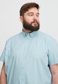 Cămașă cu mânecă scurtă, de culoare bleu deschis, din bumbac fin. Prezintă un guler clasic și o închidere cu butoane, cu butoane mici, asortate.