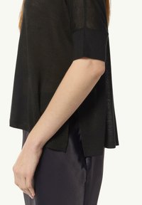 Czarny, półprzezroczysty top z krótkim rękawem o luźnym kroju. Posiada boczny rozcięcie i teksturowany materiał, zestawiony z gładką, ciemną satynową spódnicą.