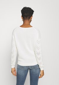 White sweater with a textured body and open-knit chevron pattern on the sleeves. Ribbed cuffs and hem; relaxed fit; lightweight material.