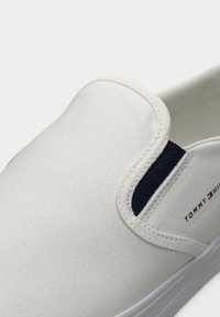 Baskets blanches à enfiler avec panneau latéral élastique et logo Tommy Hilfiger sur le côté au-dessus de la semelle.