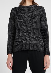 Svart och silver stickad tröja med ett strukturerat vågmönster, ribbad halsringning och muddar, samt en avslappnad passform.