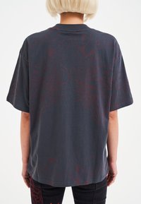 Přesně padnoucí černé tričko s grafickým motivem lva v bordó barvě a textovými detaily. Krátké rukávy a měkký bavlněný materiál, s kulatým výstřihem.