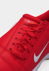 Κόκκινο αθλητικό παπούτσι με σατέν κόκκινα κορδόνια, λευκό λογότυπο Nike στο πλευρό και κείμενο «total one» κοντά στη μαλακή γλώσσα.