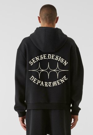 Felpa nera con vestibilità rilassata, caratterizzata dalla scritta bianca "SENSE.DESIGN DEPARTMENT" e linee decorative sul retro. Materiale morbido, polsini a coste.