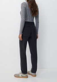 Haut gris à manches longues à rayures associé à un pantalon taille haute bleu foncé avec des poches arrière. Les chaussures sont grises avec des accents blancs et beiges.