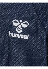 Granatowy materiał w diamentowy wzór; zawiera białe, haftowane logo pszczoły oraz tekst "hummel", umieszczony po lewej stronie.