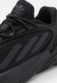 Scarpa sportiva nera con collo imbottito, tomaia in tessuto testurizzato e suola in gomma. Presenta tre strisce diagonali e un design con lacci.