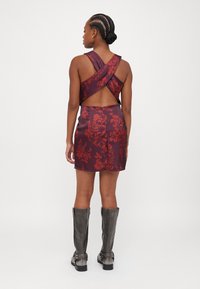 Red floral patterned satin dress with an open back and crossed straps. Paired with knee-high gray leather boots.