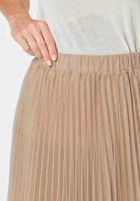 Plisseerok in beige, gemaakt van lichte stof met een elastische tailleband, met verticale plooien en een soepele textuur.