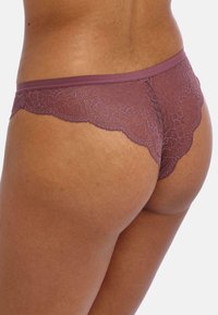 Lace stringtanga in mauve met een geschulpte rand. Zachte, doorschijnende textuur met bloemenpatronen en een gladde tailleband.