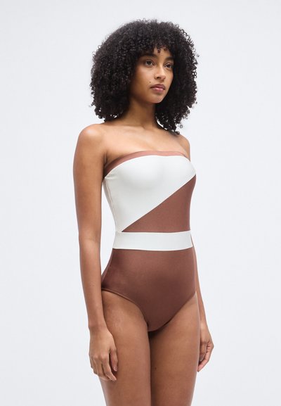 Pánt nélküli egyrészes fürdőruha színblokkolt kialakítással: fehér felső rész, barna alsó rész és hangsúlyos szalag. Simaságú, rugalmas anyagból készült.