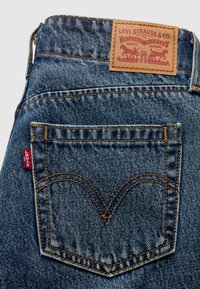 Poche arrière d'un jean Levi's bleu avec coutures orange, étiquette rouge Levi's et étiquette de marque en cuir marron Levi Strauss & Co. sur la ceinture.