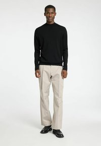 Schwarzer, langärmeliger Strickpullover kombiniert mit beigen, taillierten Hosen und schwarzen Schuhen. Einfaches Design, strukturierter Stoff und neutrale Farbpalette.