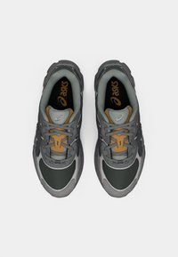 Ζευγάρι γκρι και μαύρες παπούτσια τρεξίματος ASICS με μπεζ λεπτομέρειες, απεικονιζόμενο από πάνω σε λευκό φόντο.