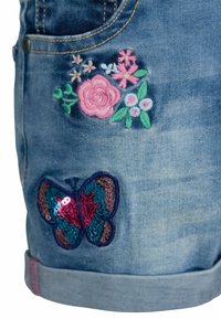 Jeansshorts med broderade rosa och vita blommor ovanför en blå och rosa pailletterad fjärilspatch nära den fållade kanten.