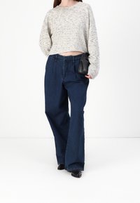 Sweter w stylu na szydełku w kremowym kolorze, z długimi rękawami i krótkim krojem, zestawiony z szerokimi, granatowymi jeansami i małą czarną torebką.