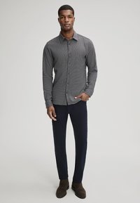 Grijs geruit overhemd met een spitse kraag, gedragen met marineblauwe broek en bruine enkellaarzen. Gladde stof textuur, slim fit.