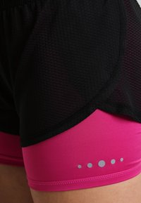 Pantalones cortos de malla negros con una capa inferior rosa, que presentan un dobladillo redondeado y acentos de puntos plateados en el lado inferior.