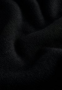 Černá látka s texturovaným, tkaným povrchem, zobrazující měkké záhyby a jemné vzory. Materiál působí teple a útulně, ideální pro zimní oblečení.