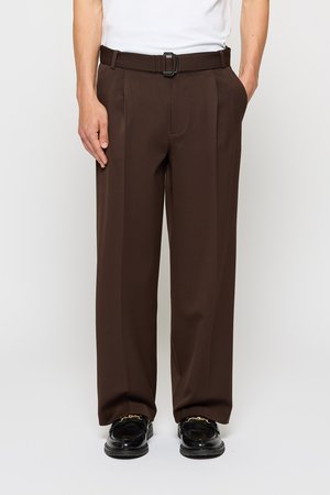 Brown tailored trousers with a high waist, featuring front pleats and a black buckle belt. Smooth texture complements polished shoes.