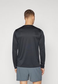 Svart långärmad träningströja i mjukt, lätt tyg; har rund hals och är ihop med grå shorts.
