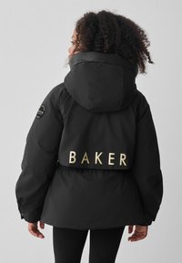Črna puhovka s kapuco, z zlatim napisom "BAKER" na hrbtni strani in krožnim logotipom na levem rokavu. Gladek, strukturiran material.