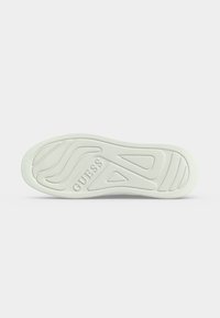 Semelle de chaussure en caoutchouc blanc avec motifs texturés pour une bonne adhérence et le nom de la marque « GUESS » embossé au centre.