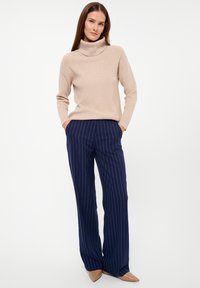 Beige turtleneck sweater made of knit fabric, paired with navy blue pinstriped trousers. Trousers have a loose fit and a straight leg design.