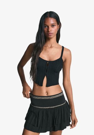 Black ribbed tank top with a front keyhole detail, paired with a black ruffled skirt featuring a studded waistband.