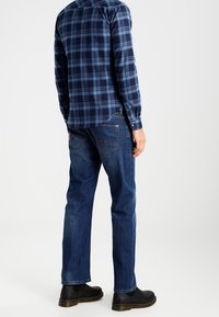 Granatowa koszula flanelowa w kratę z długimi rękawami, zestawiona z ciemnymi dżinsami o prostym kroju i czarnymi botkami za kostkę.