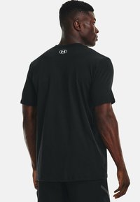 T-shirt atletico nero con maniche corte, scollo a giro e logo Under Armour sulla schiena. Realizzato in tessuto morbido e traspirante.