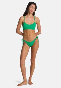Σετ πράσινου μπικίνι με αδιάκοπο cropped τοπ με λεπτές τιράντες και χαμηλόμεσο σορτσάκι με πλαϊνά κέτσα να δένουν. Ομαλό, ελαστικό ύφασμα.
