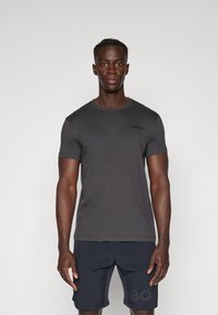Tricou ajustat de culoare gri închis, cu mâneci scurte, decolteu rotund și un detaliu mic de branding. Asortat cu pantaloni scurți bleumarin cu imprimeu logo.