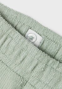 Tissu en tricot doux et côtelé de couleur vert clair avec une surface texturée et une fermeture à bouton blanc sur un fond en tissu beige.