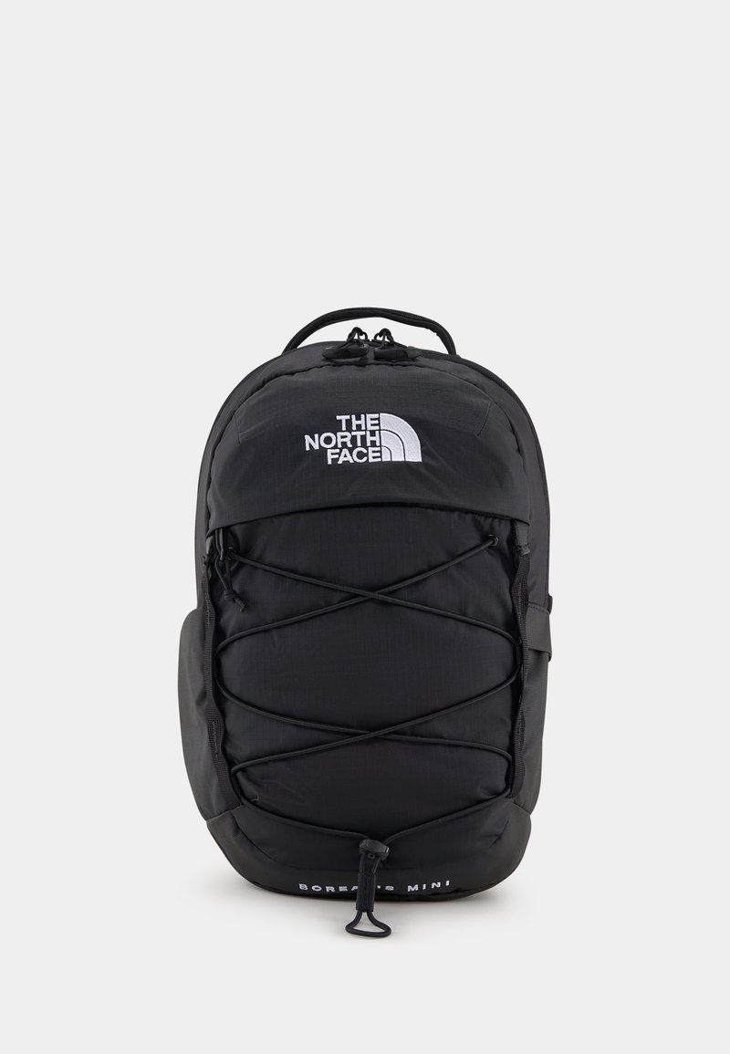Sac à dos noir avec structure rembourrée, logo à l'avant, cordon élastique bungee et bretelles ajustables. Comprend une poche zippée sur le côté.