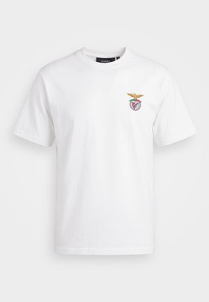 Άσπρη κοντομάνικη μπλούζα με στρογγυλή λαιμόκοψη και ένα μικρό πολύχρωμο κεντητό έμβλημα με αετό και ασπίδα στο αριστερό μέρος του στήθους.