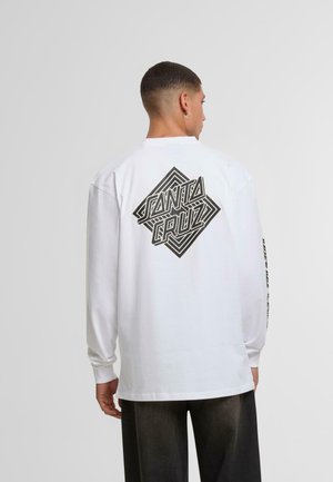 Tricou alb din bumbac cu mânecă lungă, prezentând un grafic geometric negru "Santa Cruz" pe spate și detalii textuale pe mânecă.