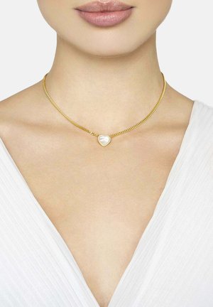 Aranylánc nyaklánc szív alakú, gyöngyházfényű medállal, sima, mezítelen nyakon pihen. Egyszerű kialakítás, minimális díszítéssel.