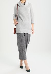 Ljust grå ribbad tröja med hög krage och trekvartsärmar, i kombination med mörkgrå strukturerade vida byxor och gröna klackar.