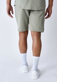 Pantaloni corti verde chiaro in cotone con una morbida texture, abbinati a calzini bianchi a coste e sneaker bianche. Presentano dettagli con tasche laterali.