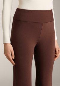 Hnedé legíny s hladkou textúrou, širokým pásom a priliehavým strihom, zobrazené spolu so svetlým dlhým rukávom.