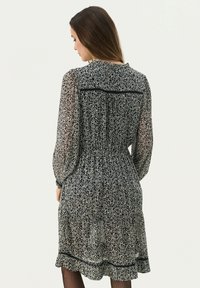 Rochie cu imprimeu floral alb-negru, cu mâneci lungi din material transparent, talie ajustată și tiv volanat. Îmbrăcată cu o bandă de accent neagră.