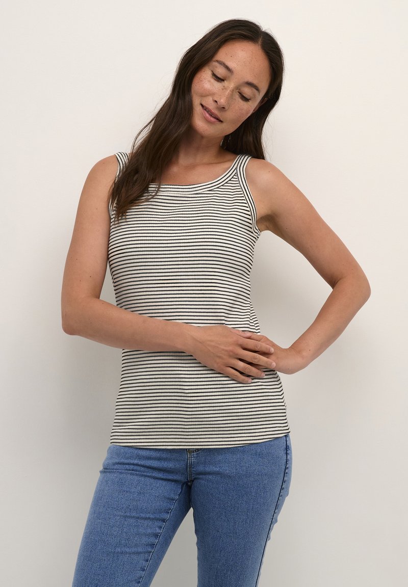 Débardeur rayé en blanc cassé et noir, avec un encolure dégagée et une coupe ajustée. Porté avec un jean bleu, mettant en avant le confort décontracté.