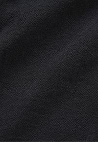 Gros plan sur un tissu noir avec un motif en losange tissé subtil et des plis doux créant texture et ombre.
